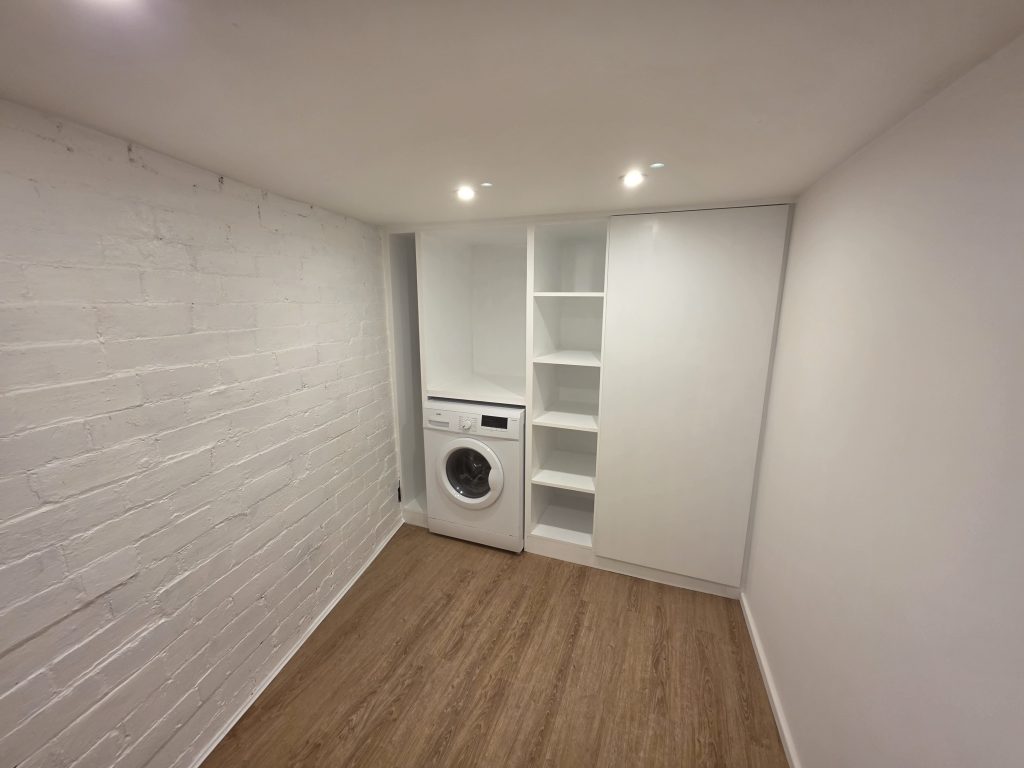Bespoke white fitted utility storage cabinetry built around washing machine
