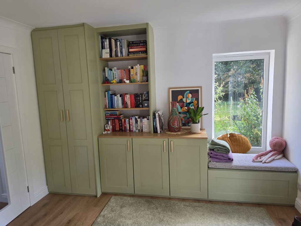 Sage-green built-in storage with a tall cupboard, open shelving and fitted window seat.