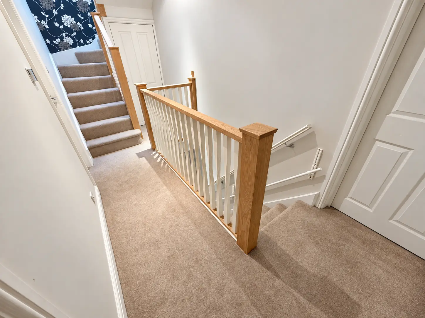 Solid oak staircase handrail and newel posts with decorative white twisted spindles on a carpeted landing in Leeds.